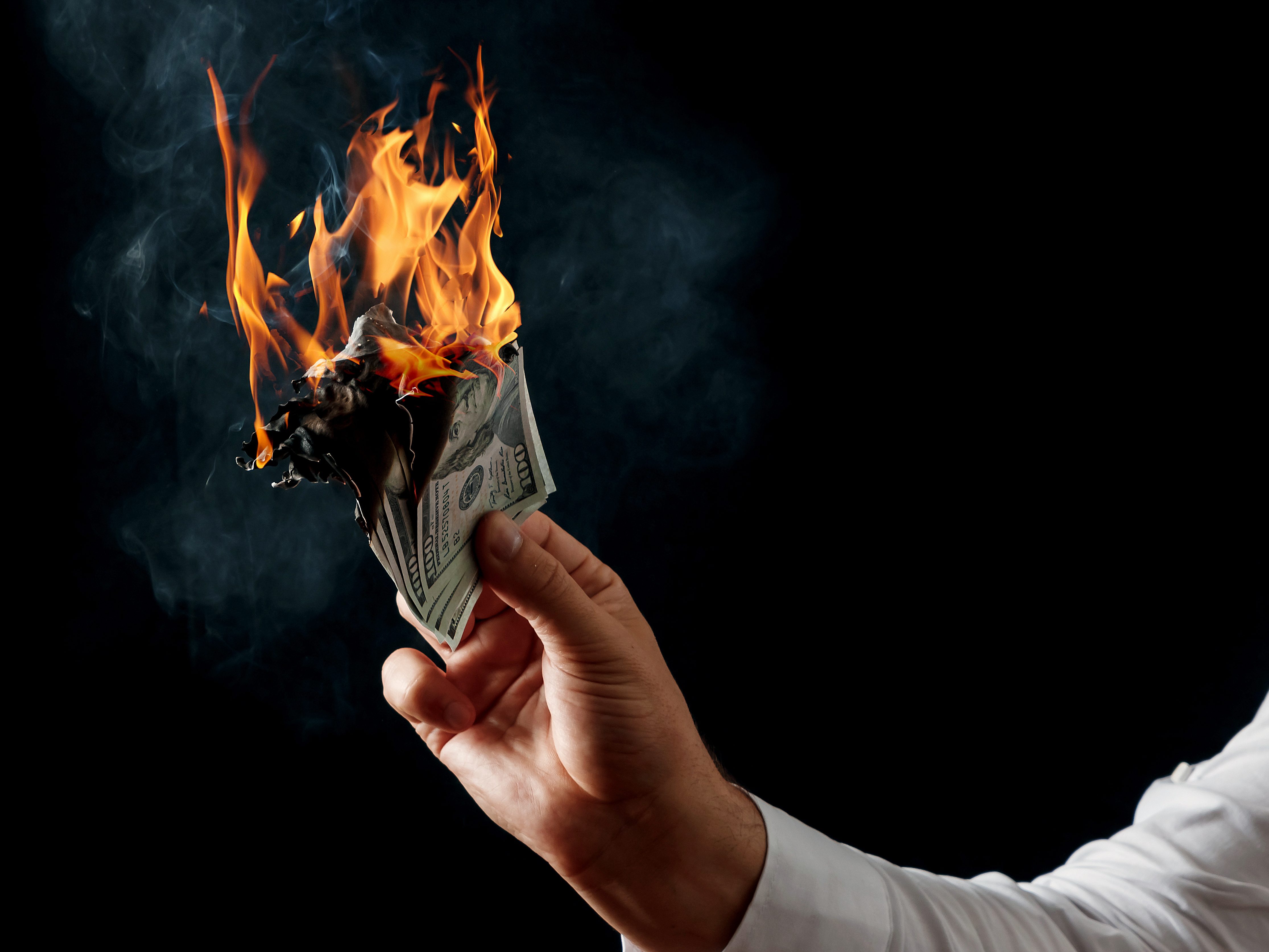 Male hand close-up, holds burning money in hands, burning US dollars. Black background, isolate. The concept of inflation, a decrease in the purchase of foreign currency, and devolution. Burning Money