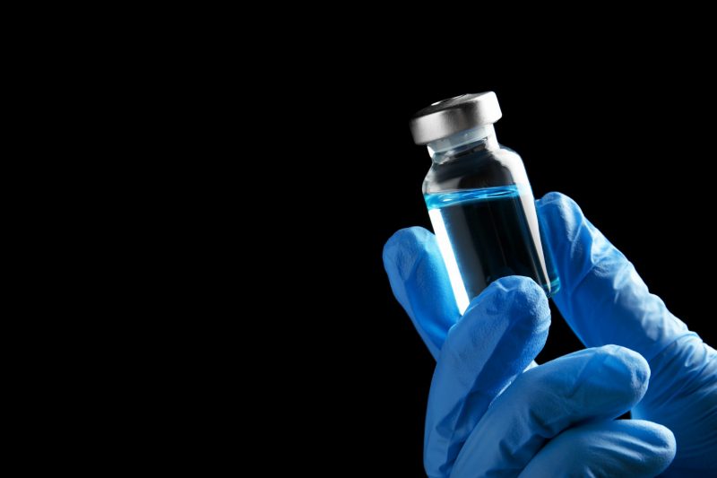 Doctor holding vial with medication on black background, closeup view and space for text. Vaccination and immunization Coronavirus Vaccine May Never Be Developed
